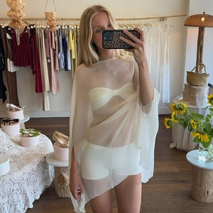 Detail view of the beige sheer mesh poncho fabric on a female model in a boutique