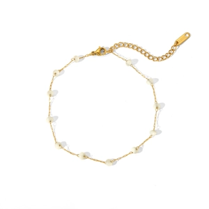 Détail d'une chevillère en acier doré avec perles blanches et chaîne d'extension réglable