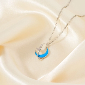 Silver crescent moon necklace with blue enamel and sparkling zircon on silk background