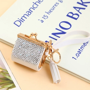 Macro detail of a white rhinestone mini bag keychain with gold clasp and tassel detail