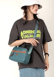 Detail of teal nylon crossbody bag featuring wide branded strap and zip compartments
