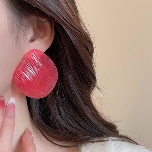 Macro view of a large red resin earring with brushed texture on a model's ear