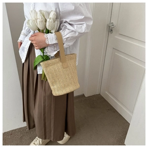 Detail of hand-woven straw bucket bag with elegant top handle and white tulips
