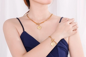 Detail of gold heart pendant necklace and bracelet set with OT buckle on a model