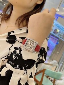 Detalle de reloj cuadrado con diamantes de imitación, correa roja y pulsera a capas