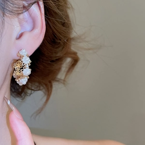 Close-up of elegant C-shaped gold earrings with 3D white flower petals on model