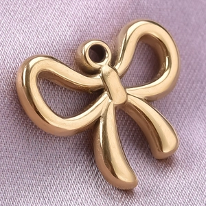 Macro view of gold stainless steel bow pendant on purple fabric for DIY jewelry
