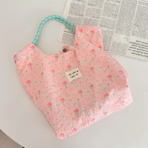 Detail of pink quilted canvas tote with rabbit tulip print and green handles on a desk