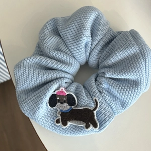 Close-up of light blue knitted scrunchie with cute black cartoon dog embroidery detail