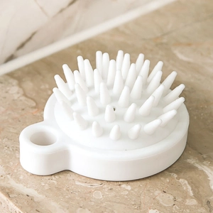 White silicone scalp massager brush with circular handle on marble surface