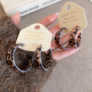 Detail shot of leopard print acrylic C-shape hoop earrings on a beige display card