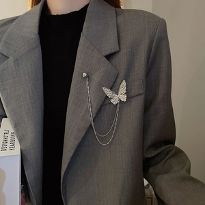 Detailed close-up of a silver butterfly brooch with double chains on a grey blazer lapel