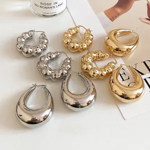 Chic gold and silver chunky teardrop hoop earrings on a minimalist background