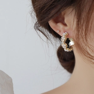 Elegant gold C-shaped hoop earrings with micro pearls and flower design worn by a model