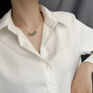 Minimalist gold necklace with three green jade beads worn on a model over a white shirt
