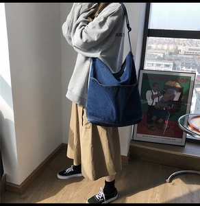Detail view of a large blue denim shoulder bag with a soft wash finish and side pockets