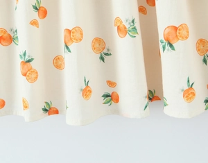 Detail of light beige summer dress showing orange fruit patterns and fabric texture
