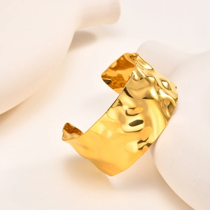 Detail of wide open gold cuff bracelet with irregular hammered texture on white ceramic base