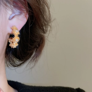 Detailed view of a gold flower C-shaped earring with zircons on a model's ear