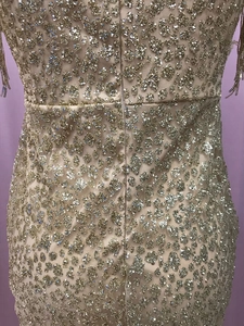 Dettaglio di paillettes dorate e nappe su un abito a sirena rosa con cerniera lampo