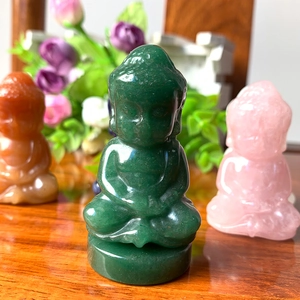 Close-up of three carved crystal Buddha statues in green orange and pink natural stone
