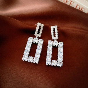 Macro shot of silver geometric square earrings with sparkling cubic zirconia on brown silk