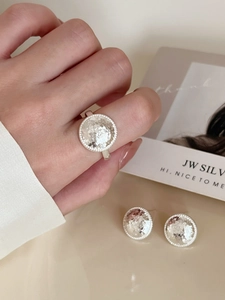 Close-up of silver geometric hammered round earrings and matching ring on model hand