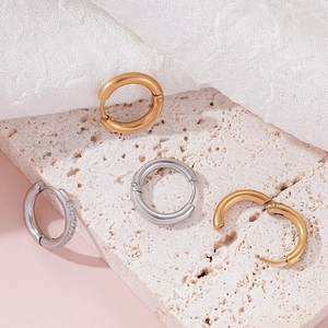 Detail view of gold and silver hoop earrings with zircon inlay on a stone surface