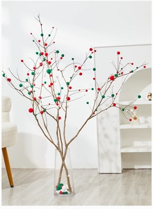Red, green, and white plush pom-poms on dry branches in a transparent glass vase