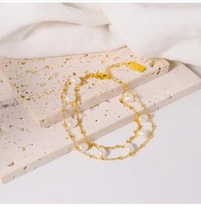 Detail view of double-layer gold pearl bracelet on a beige stone and white cloth