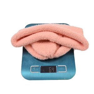Bonnet en maille peluche rose pour bébé pesant 64g sur balance montrant texture douce