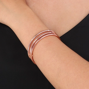 Detail of rose gold triple interlocking bangle bracelet on model wrist with metallic finish