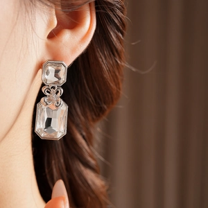 Close-up of elegant silver square crystal earrings with bow detail on female model