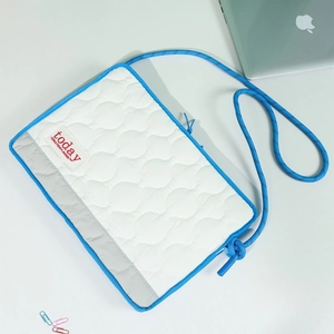 Close-up of white quilted laptop bag with blue edging and braided rope shoulder strap
