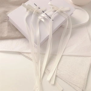 Detail of white satin double bow hair clips with long elegant ribbons on textured fabric