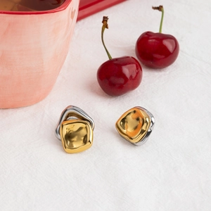 Close-up of geometric two-tone stainless steel earrings on a clean linen surface