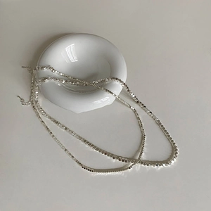 Détail d'un collier de perles facettées argentées minimalistes sur présentoir céramique