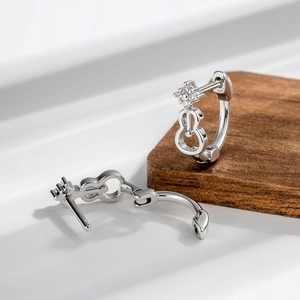 Silver violin-shaped earrings with rhinestones on a minimalist wooden display