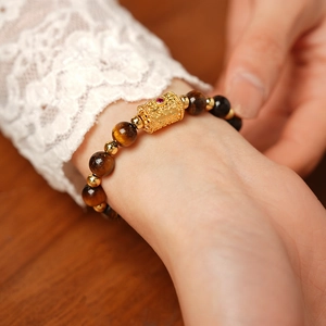 Detailed view of Tiger Eye stone beads bracelet with a gold charm on a woman's wrist