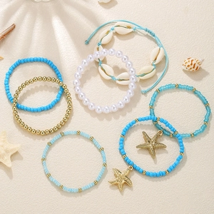 Detail of bohemian ocean beaded bracelets with shells and starfish on sandy background