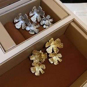 Elegant gold and silver floral stud earrings with metallic petal textures in a jewelry box