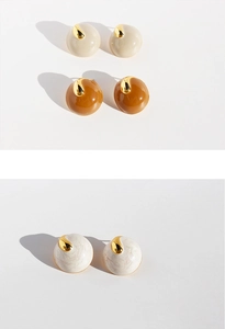 Close-up of enamel stud earrings in beige, amber and pearl white with gold accents