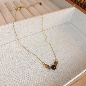 Close-up of a golden sun pendant necklace with a brown stone in a beige velvet box