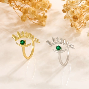 Detail of gold and silver evil eye rings with green zircon stones on soft beige background