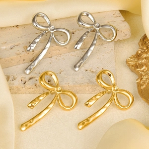 Detailed view of bow knot stud earrings in gold and silver finishes on silk fabric