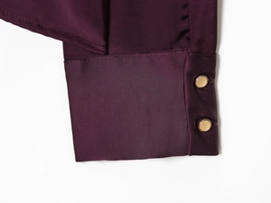 Détail de la manchette en satin bordeaux avec boutons dorés et texture soyeuse
