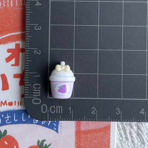Close-up of mini resin grape juice cup charm with yellow bow and cm measurement scale