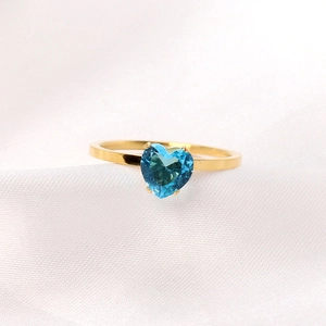 Macro shot of gold stainless steel ring featuring a heart-shaped blue gemstone on silk