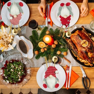 Three Christmas gnome cutlery holders with red stripes on a festive wooden dinner table