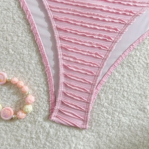 Detail of pink bikini bottom with ruched fabric and wavy scalloped edges on white rug